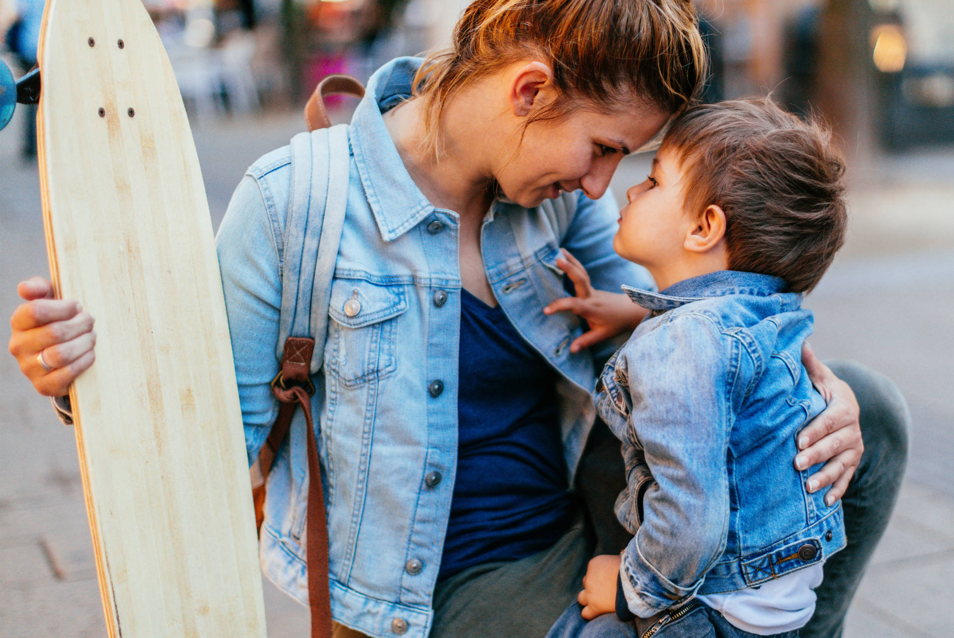 Photo of a young mother and her little boy, sharing some love and affection after skateboard ride in the city